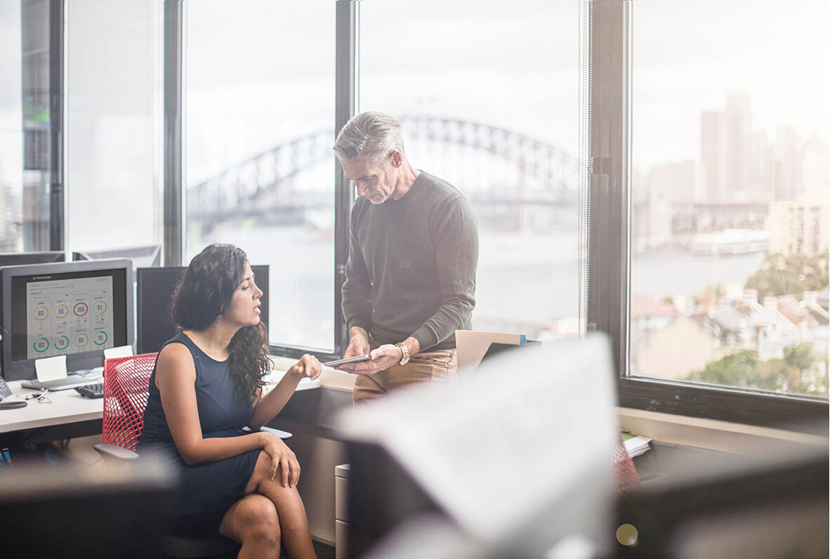 Two senior leaders have a discussion within their head office. On screen is a Teamgage report showing organisation results.